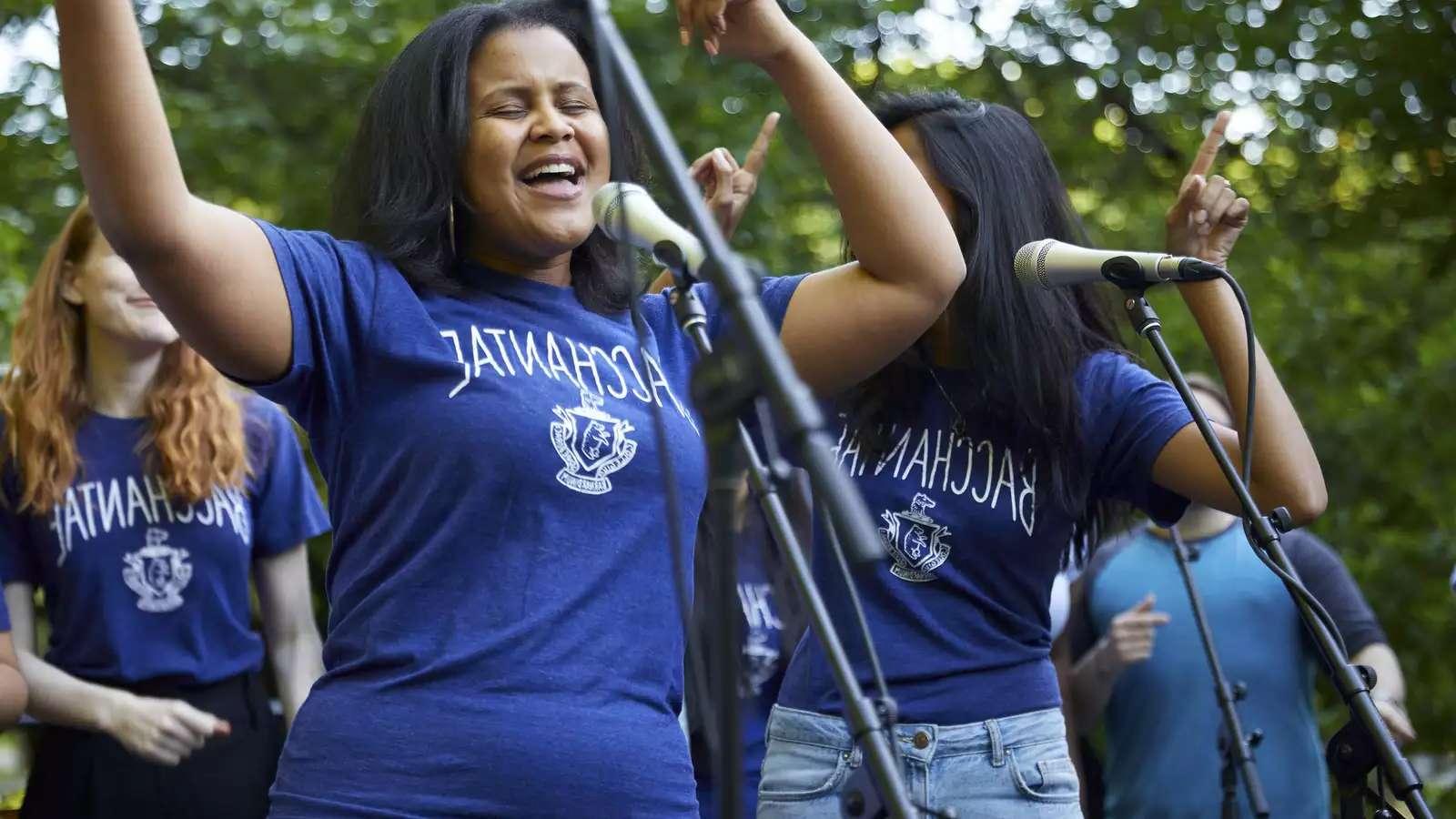 A young Black woman sings outdoors as part of the Bacchantae performance